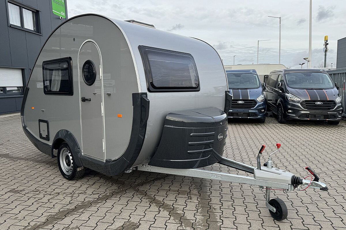 Ein kleiner, silberner Wohnwagen mit einer runden Form auf einem Parkplatz.