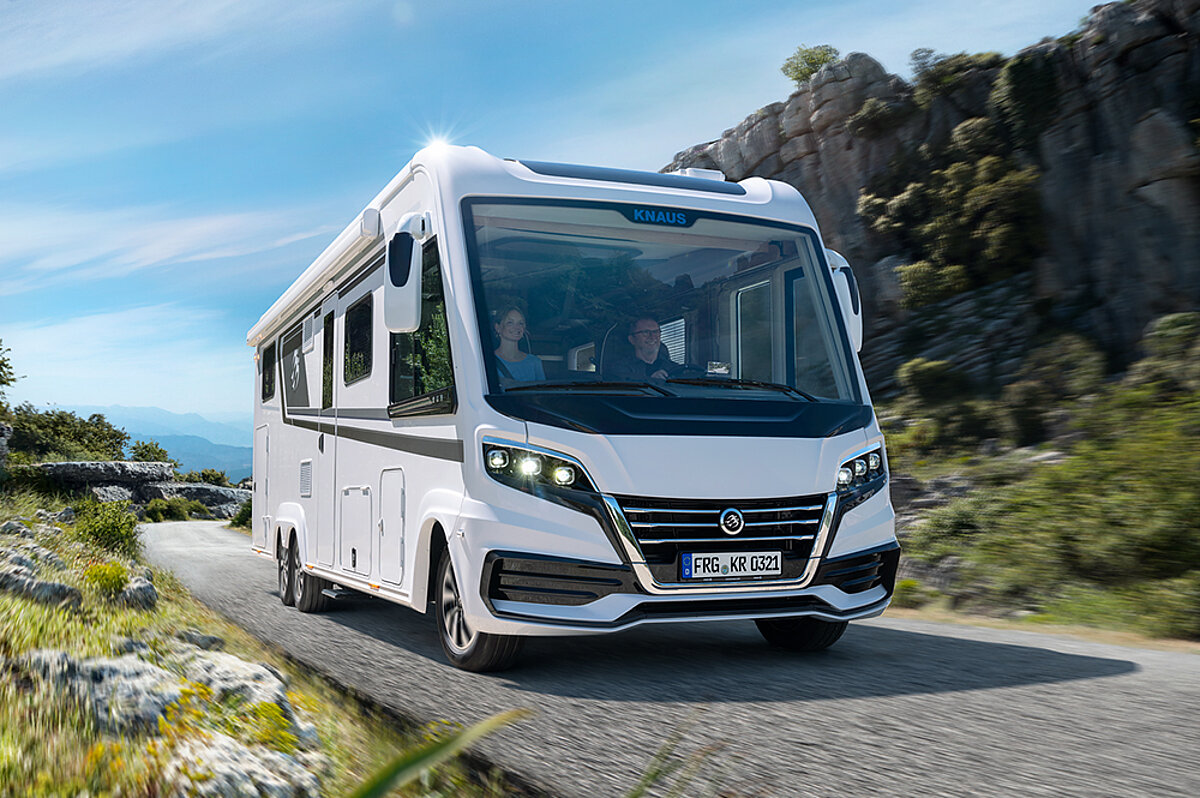 Die Freiheit des Wohnmobilurlaubs besteht darin, spontane Entscheidungen zu treffen und neue Wege zu erkunden. Zwei Personen sitzen in einem vollintegrierten Wohnmobil und fahren durch eine Landschaft.