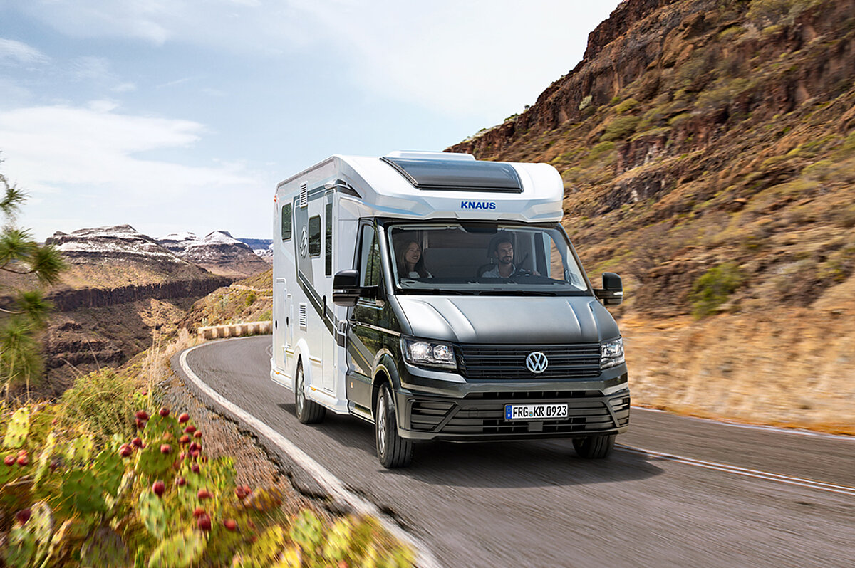 Mit dem Wohnmobil die Freiheit genießen, jeden Tag einen neuen Ort zu entdecken. Wohnmobil mit grauen Details auf einer Straße in einer kargen Landschaft.