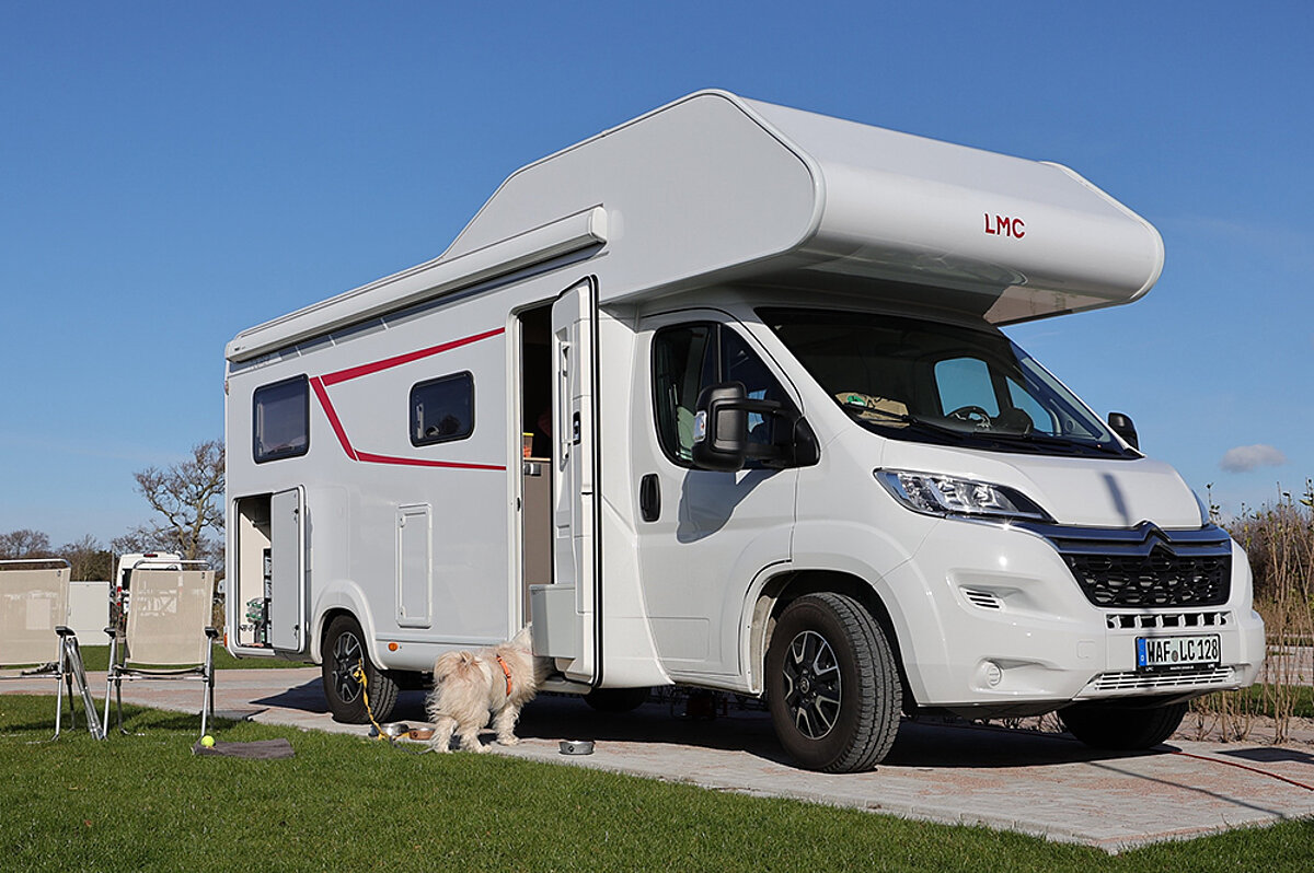Wohnwagen mit einem Hund und zwei Stühlen davor.