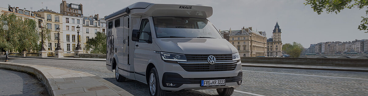 Ein kompaktes Wohnmobil steht vor einer historischen Stadt.