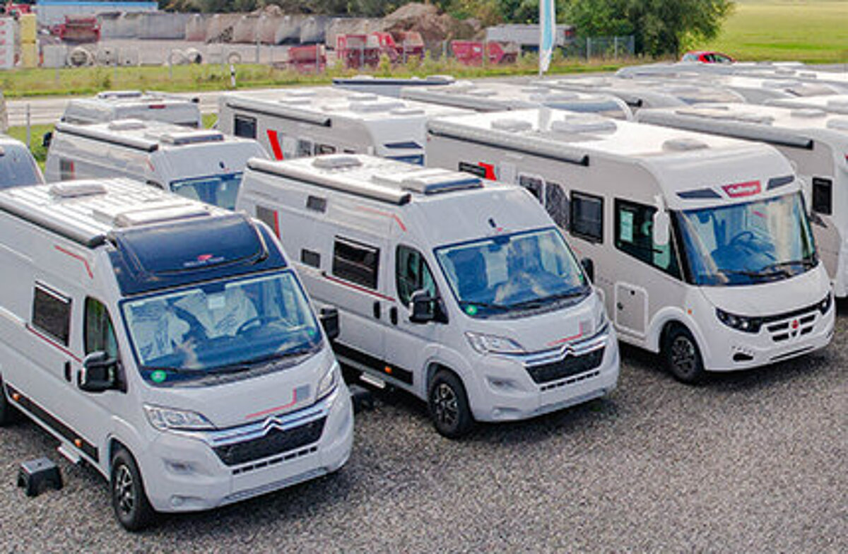 Mehrere Wohnmobile auf einem Schottervorplatz.