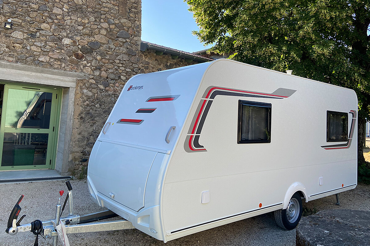 Ein Urlaub im Wohnwagen bietet die perfekte Balance zwischen Abenteuer und Komfort. Ein weißer Wohnwagen, welcher vor einer Hausfassade steht.