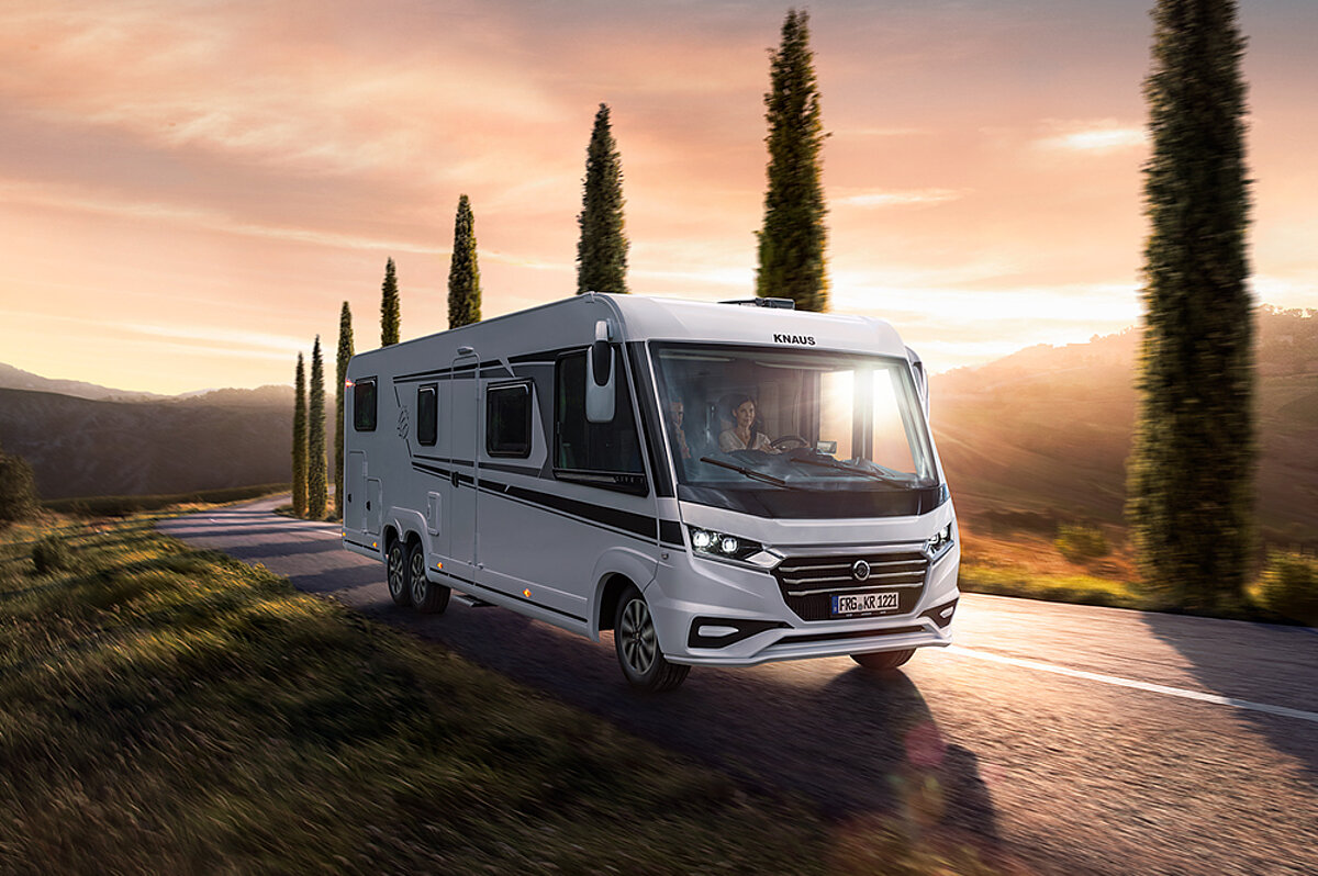 Flexibles Reisen bedeutet, die Freiheit zu haben, immer wieder neue Horizonte zu entdecken und sich vom Leben treiben zu lassen. Vollintegriertes weißes Wohnmobil auf einer Landstraße vor untergehender Sonne.