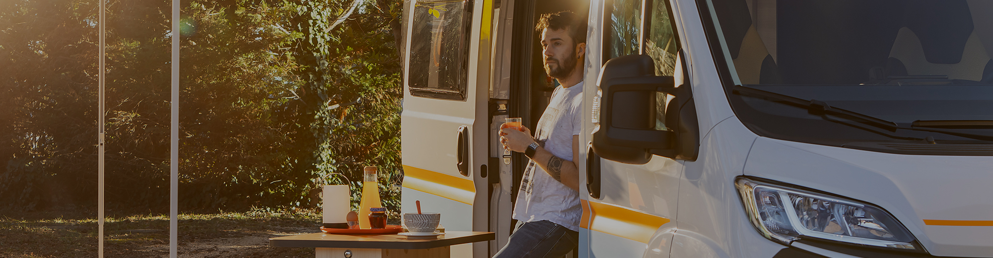 Mann steht in der geöffneten Tür eines Wohnmobil und hat eine Tasse in der Hand.