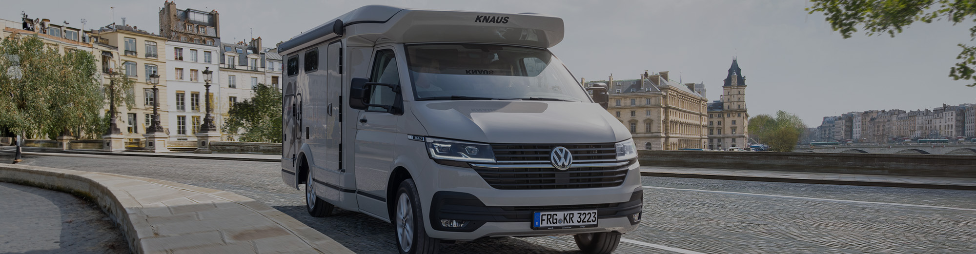 Ein kompaktes Wohnmobil steht vor einer historischen Stadt.