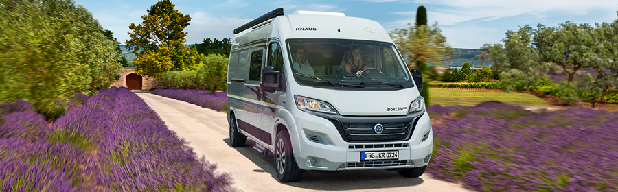 Ein Paar fährt mit einem Campervan über eine naturnahe Straße.