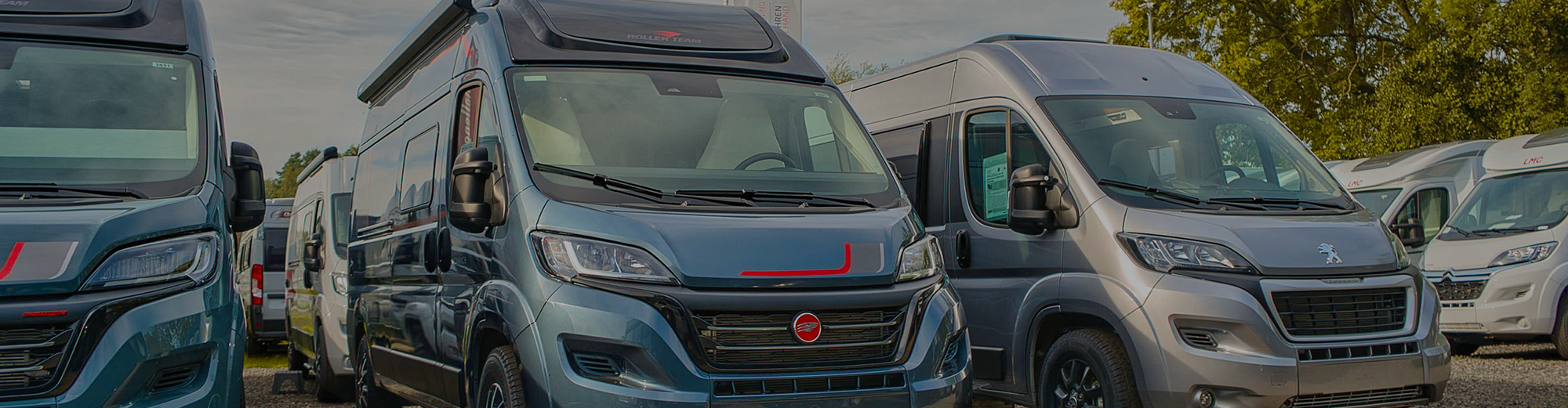 Mehrere Campervans in unterschiedlichen Designs stehen nebeneinander auf einem Parkplatz.