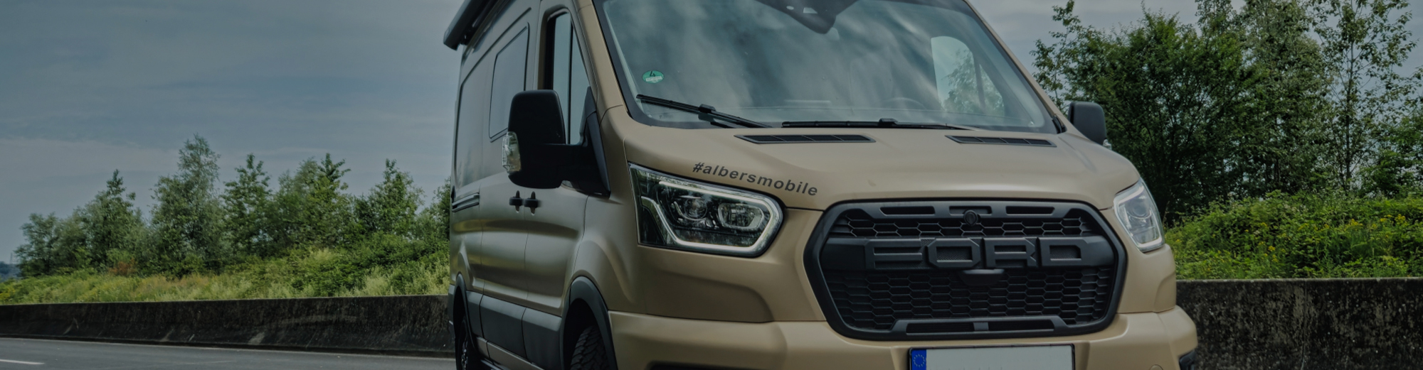 Frontansicht eines Campervans, welcher auf einer Straße fährt.