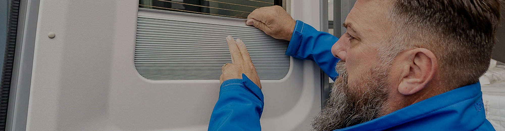 Ein Mann in einer blauen Jacke arbeitet an einem Fenster eines Wohnmobils.